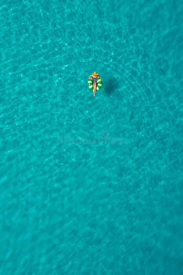 Aerial view of slim woman swimming on the swim ring donut in the transparent turquoise sea in Seychelles. Summer seascape with girl, beautiful waves, colorful water. Top view from drone. Aerial view of slim woman swimming on the swim ring donut in the transparent turquoise sea in Seychelles. Summer seascape with girl, beautiful waves, colorful water. Top view from drone