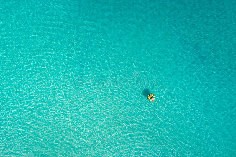 Aerial view of slim woman swimming on the swim ring  donut in the transparent turquoise sea in Seychelles. Summer seascape with girl, beautiful waves, colorful water. Top view from drone. Aerial view of slim woman swimming on the swim ring  donut in the transparent turquoise sea in Seychelles. Summer seascape with girl, beautiful waves, colorful water. Top view from drone