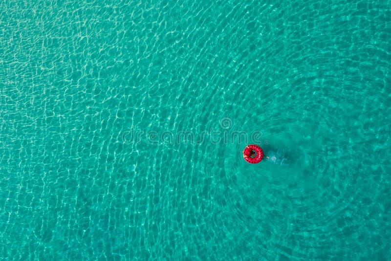 Aerial view of slim woman swimming on the swim ring  donut in the transparent turquoise sea in Seychelles. Summer seascape with girl, beautiful waves, colorful water. Top view from drone. Aerial view of slim woman swimming on the swim ring  donut in the transparent turquoise sea in Seychelles. Summer seascape with girl, beautiful waves, colorful water. Top view from drone