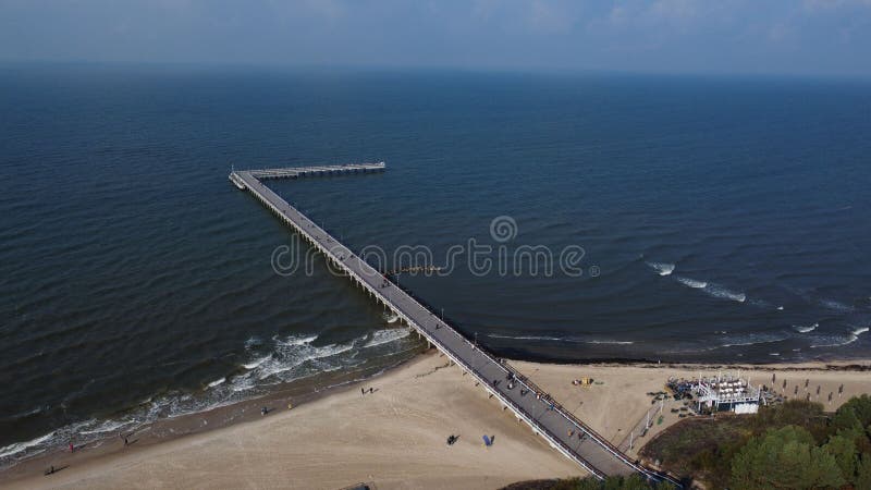 Una vista aérea de un puente que une la costa con un océano en el que la gente camina