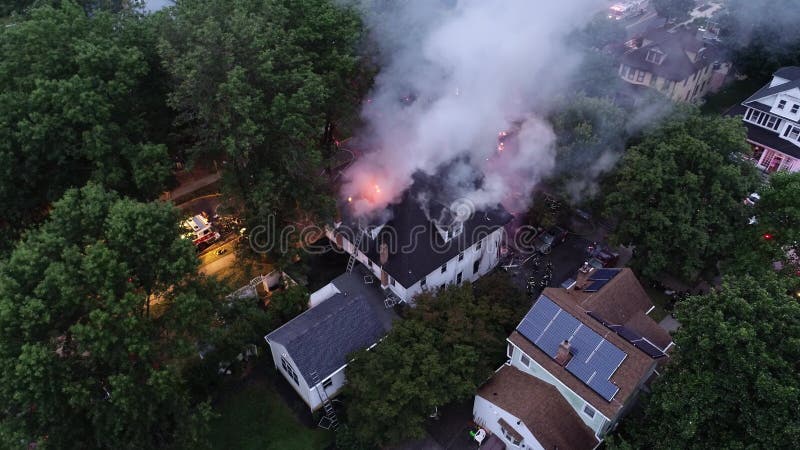 Vista aérea dos carros de bombeiros e do instrumento que lutam um fogo da casa