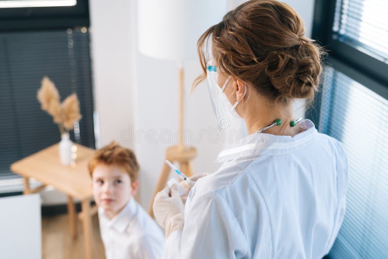 Vista dal retro di una donna dottoressa irriconoscibile in guanti di lattice che preparano un vaccino per bambini in ospedale con fotografie stock