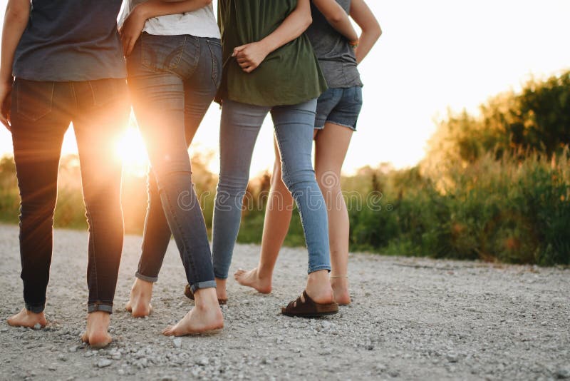 Vista de atrás de un grupo de amigas abrazándose y caminando al aire libre en un día soleado imagen de archivo