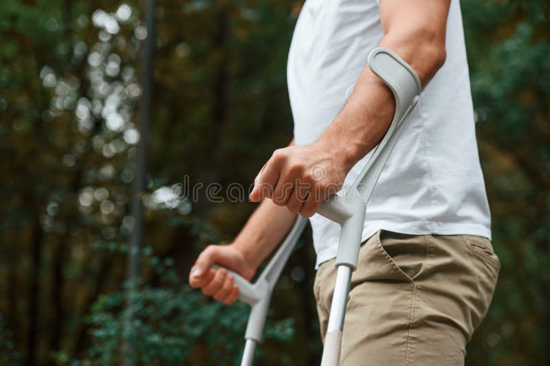 Vista de cierre. hombre con muletas está en el parque al aire libre. lesión en la pierna imagen de archivo