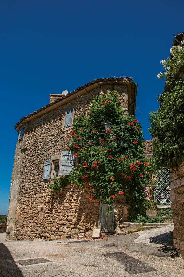 Vista de la casa de piedra típica con el cielo azul y las flores soleados, en un callejón del pueblo histórico de Menerbes fotos de archivo libres de regalías Vista de la casa de piedra típica con el cielo azul y las flores soleados, en un callejón del pueblo histórico de Menerbes fotos de archivo libres de regalías