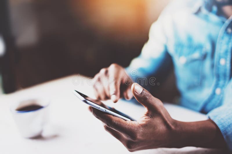 Vista del primo piano delle mani maschii che toccano telefono cellulare Uomo africano che per mezzo dello smartphone mentre seden fotografia stock Vista del primo piano delle mani maschii che toccano telefono cellulare Uomo africano che per mezzo dello smartphone mentre seden fotografia stock