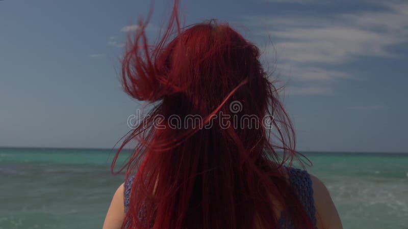 Vista della parte posteriore di una donna con capelli rossi che volano nel vento contro il contesto della spuma del mare