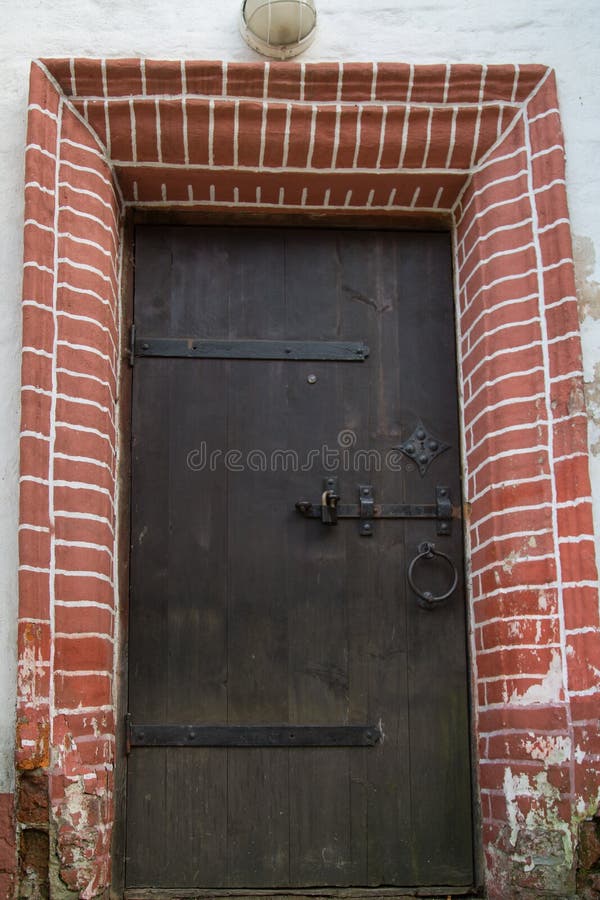 Vista della vecchia porta di legno, cerniere di metallo fucinate, serrature, bellissima finitura decorativa con mattoni Architett immagine stock libera da diritti Vista della vecchia porta di legno, cerniere di metallo fucinate, serrature, bellissima finitura decorativa con mattoni Architett immagine stock libera da diritti