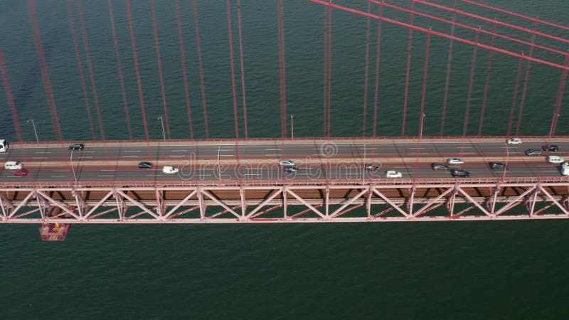 Vista deslizante lateral del tráfico ocupado de múltiples carriles a través de un puente rojo sobre el mar. coches cruce ponte 25 almacen de video