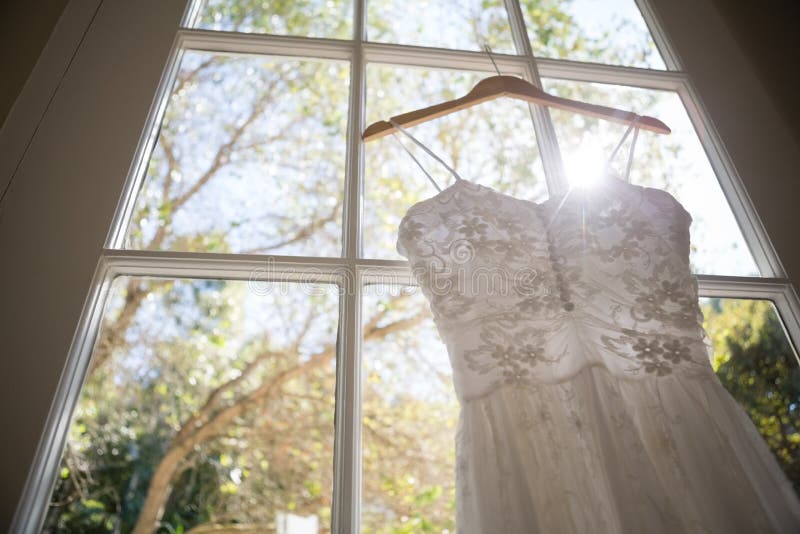 Vista di angolo basso del vestito da sposa che appende sulla finestra nella sala fotografia stock libera da diritti Vista di angolo basso del vestito da sposa che appende sulla finestra nella sala fotografia stock libera da diritti