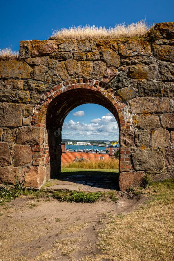 Vista di estate tramite un vecchio portone incurvato medievale della parete di pietra alla fortezza di Varberg in Svezia con la c fotografie stock Vista di estate tramite un vecchio portone incurvato medievale della parete di pietra alla fortezza di Varberg in Svezia con la c fotografie stock