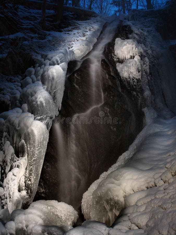 Vista di inverno di notte alla cascata congelata, ai ghiaccioli ed ai massi ghiacciati nella corrente. immagine stock Vista di inverno di notte alla cascata congelata, ai ghiaccioli ed ai massi ghiacciati nella corrente. immagine stock