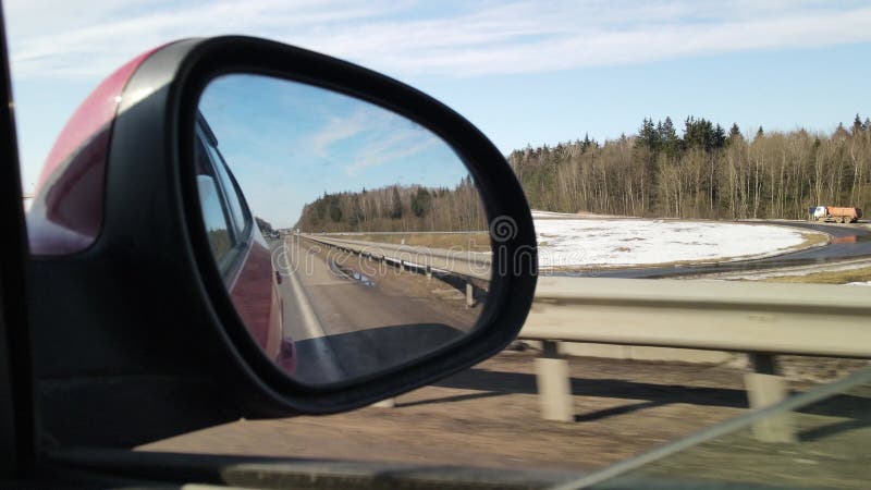 Vista en el retrovisor lateral de un auto conduciendo un auto rojo