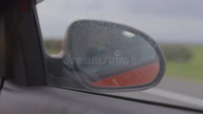 Vista en el retrovisor lateral de un auto conduciendo un auto rojo