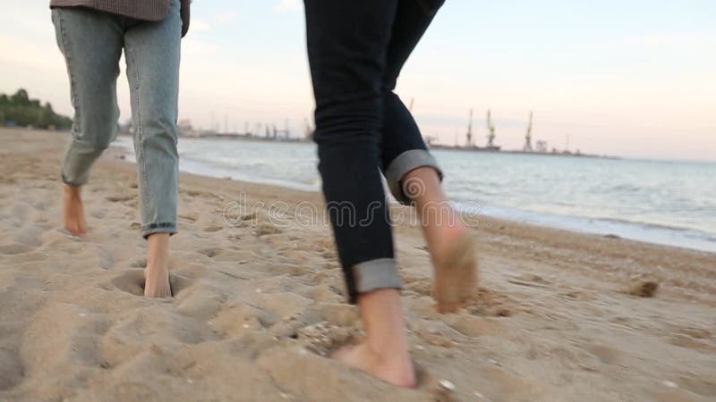 Vista en ángulo bajo, romántica, de dos pies sobre la arena, cogidos de la mano en la playa cerca del mar en cámara lenta. novio