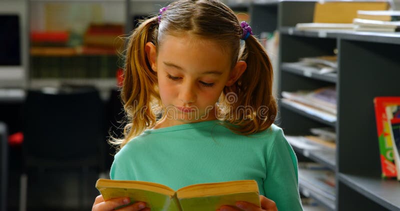 Vista frontale della scolara caucasica attenta che legge un libro in biblioteca alla scuola 4k