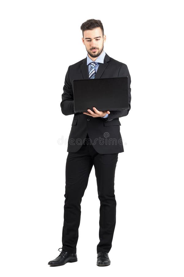 Vista frontale di giovane uomo corporativo barbuto che lavora al computer portatile fotografia stock Vista frontale di giovane uomo corporativo barbuto che lavora al computer portatile fotografia stock