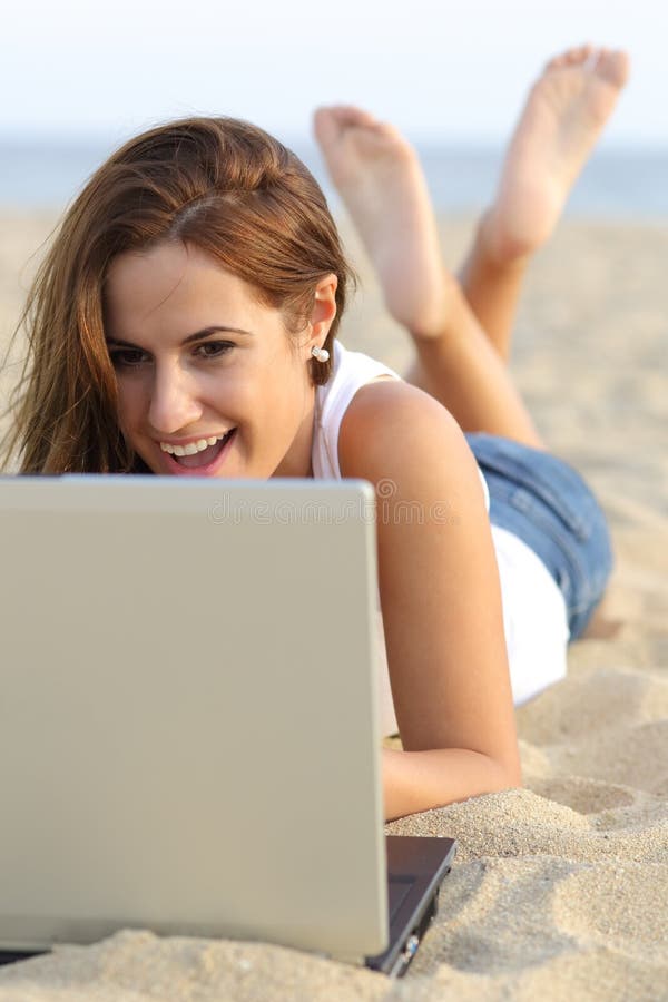 Vista frontale di una ragazza dell'adolescente che passa in rassegna il suo computer portatile che si trova sulla sabbia della spi immagine stock libera da diritti Vista frontale di una ragazza dell'adolescente che passa in rassegna il suo computer portatile che si trova sulla sabbia della spi immagine stock libera da diritti