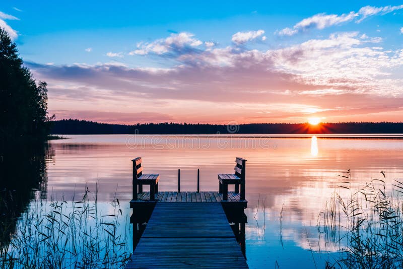 Vista idilliaca del pilastro lungo con il banco di legno sul lago Tramonto o alba sopra l'acqua fotografia stock Vista idilliaca del pilastro lungo con il banco di legno sul lago Tramonto o alba sopra l'acqua fotografia stock