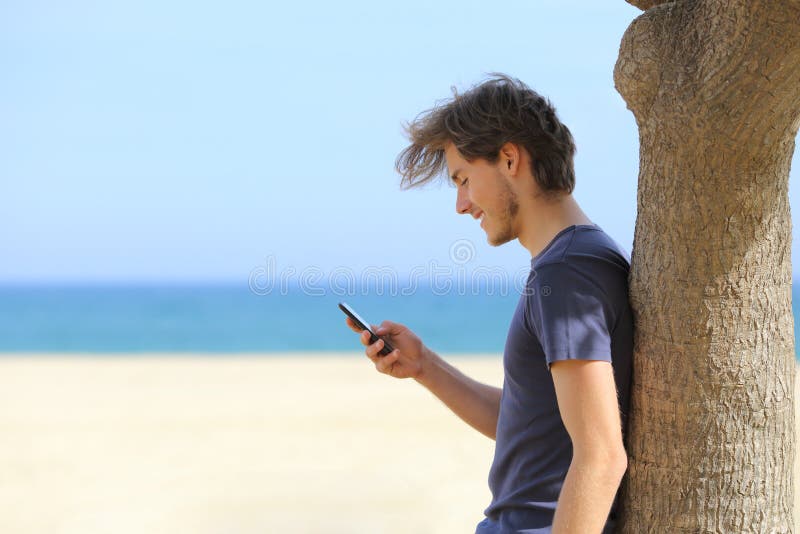 Vista lateral de un hombre atractivo que usa un teléfono elegante en la playa imagen de archivo Vista lateral de un hombre atractivo que usa un teléfono elegante en la playa imagen de archivo