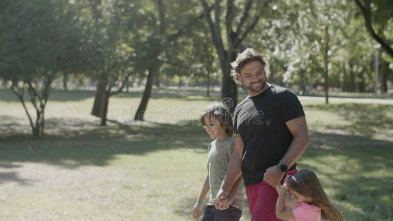 Vista lateral de un hombre discapacitado paseando con niños en el parque almacen de metraje de vídeo