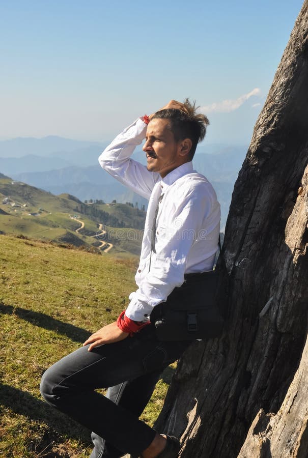 Vista lateral de un joven apuesto que se mueve la mano sobre el pelo con un árbol en la montaña foto de archivo libre de regalías