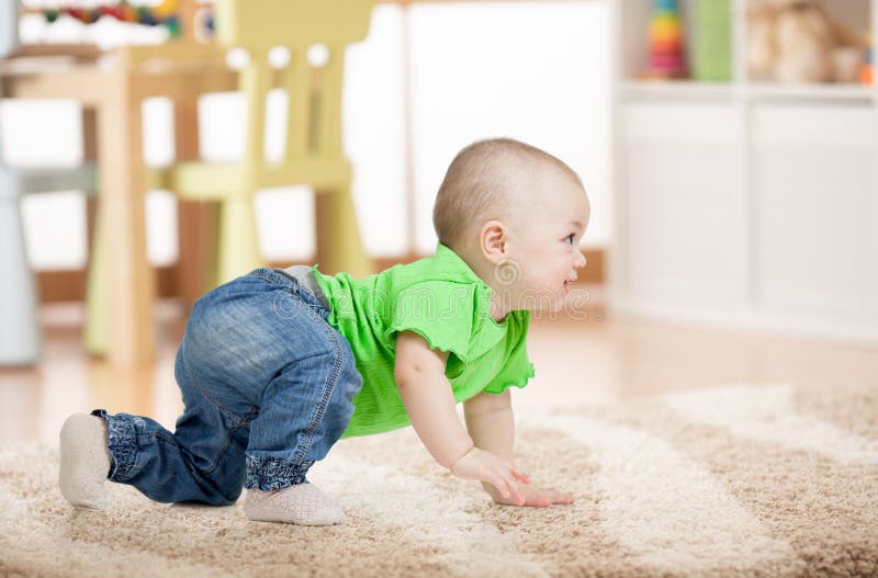 Vista lateral del bebé que se arrastra en la alfombra en piso en sitio de niños