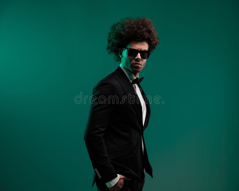 Vista lateral del elegante hombre de moda con pelo rizado posando con la mano en los bolsillos imágenes de archivo libres de regalías