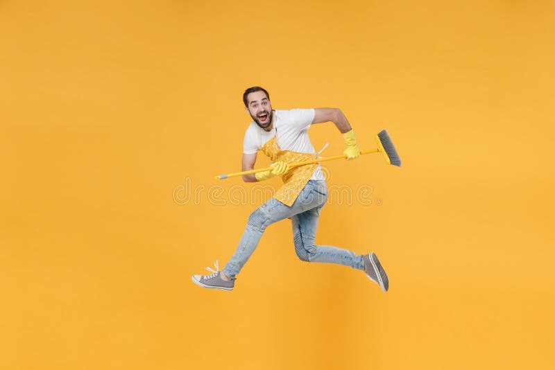 Vista lateral del excitado joven ama de casa loco en los guantes de goma de manzana sujete en la escoba de las manos mientras real imágenes de archivo libres de regalías