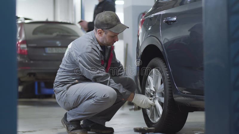 Vista lateral dos parafusos de aperto para profissionais adultos na roda do carro. mecânico de automóveis masculino caucasiano que