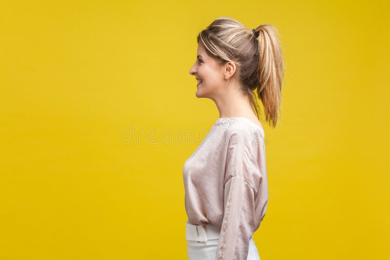 Vista laterale del profilo di una giovane donna allegra e soddisfatta con capelli da favola e camicetta di beige, isolata in gial immagini stock