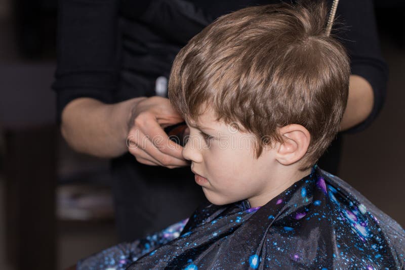 Vista laterale del ragazzino sveglio che ottiene taglio di capelli dal parrucchiere alla t fotografia stock libera da diritti Vista laterale del ragazzino sveglio che ottiene taglio di capelli dal parrucchiere alla t fotografia stock libera da diritti