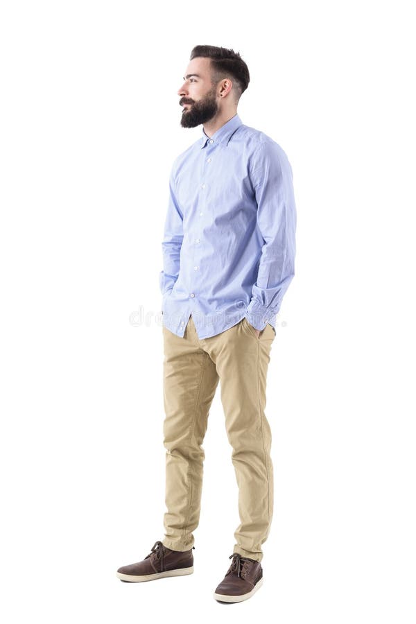 Vista laterale dell'uomo barbuto bello elegante di affari che cerca sorridente con le mani in tasche immagine stock Vista laterale dell'uomo barbuto bello elegante di affari che cerca sorridente con le mani in tasche immagine stock