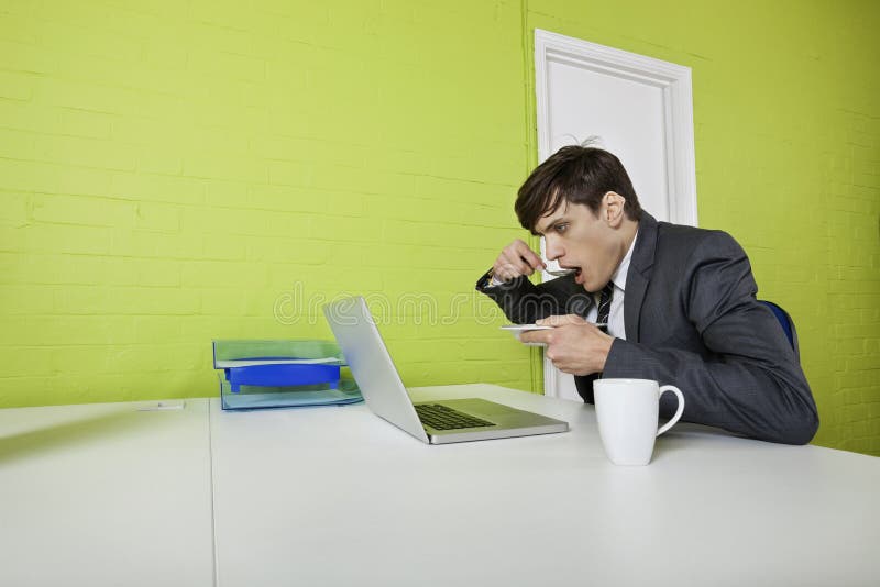 Vista laterale di giovane uomo d'affari che mangia mentre per mezzo del computer portatile alla tavola immagine stock libera da diritti