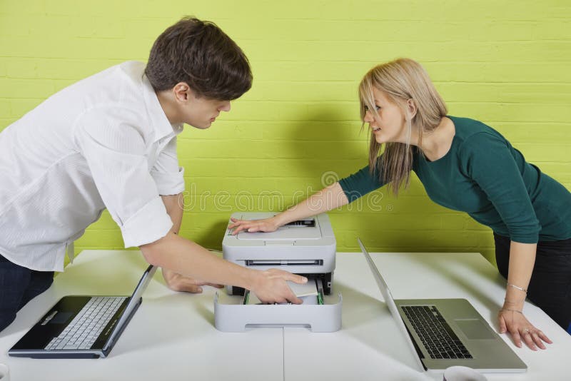 Vista laterale di giovani persone di affari che installano stampante con i computer portatili allo scrittorio fotografia stock libera da diritti