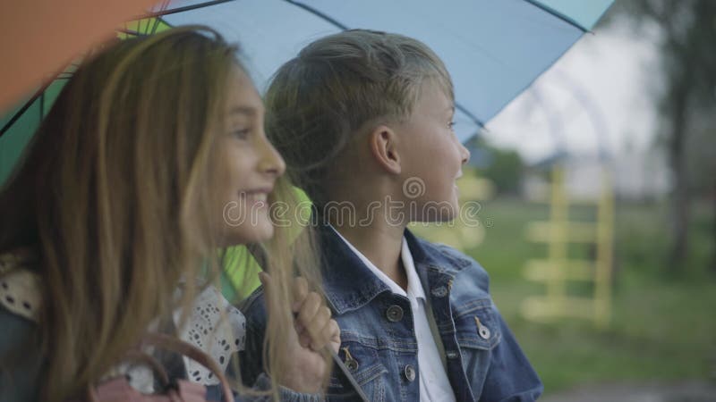 Vista laterale di un bel ragazzo romantico seduto con una ragazza sotto un ombrello colorato e parla. ragazzo caucasico che esce c