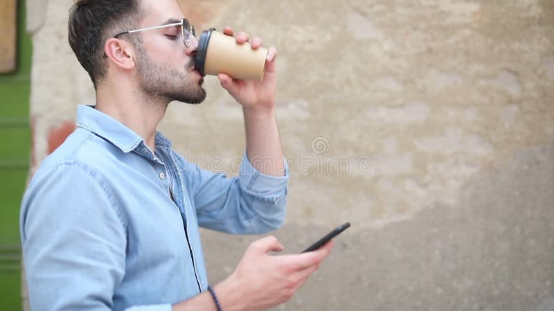 Vista laterale di un caffè bevente del giovane uomo casuale mentre per mezzo del telefono