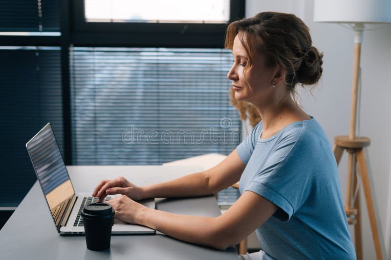Vista laterale di una donna d'affari bionda seria che lavora su computer portatile e guarda lo schermo con grande concentrazione immagini stock libere da diritti