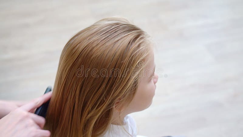 Vista laterale ragazza della scuola dolce sbadiglia mentre la madre pettina i capelli archivi video