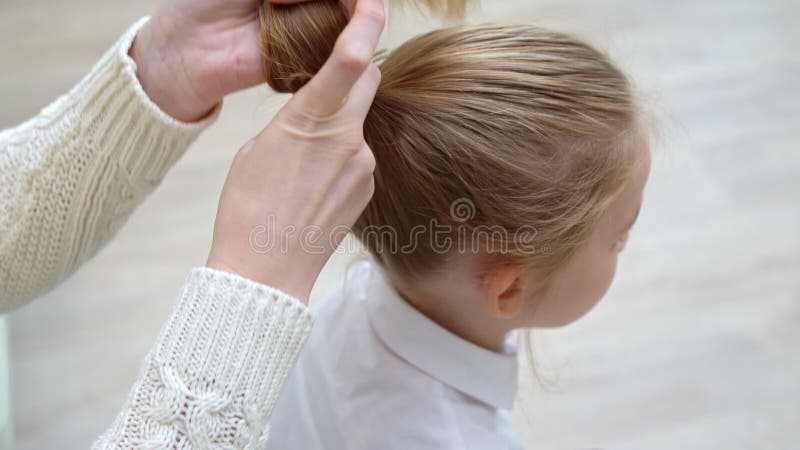 Vista laterale. ragazza della scuola dolce seduta mentre la madre pettina i capelli e li colta in coda archivi video