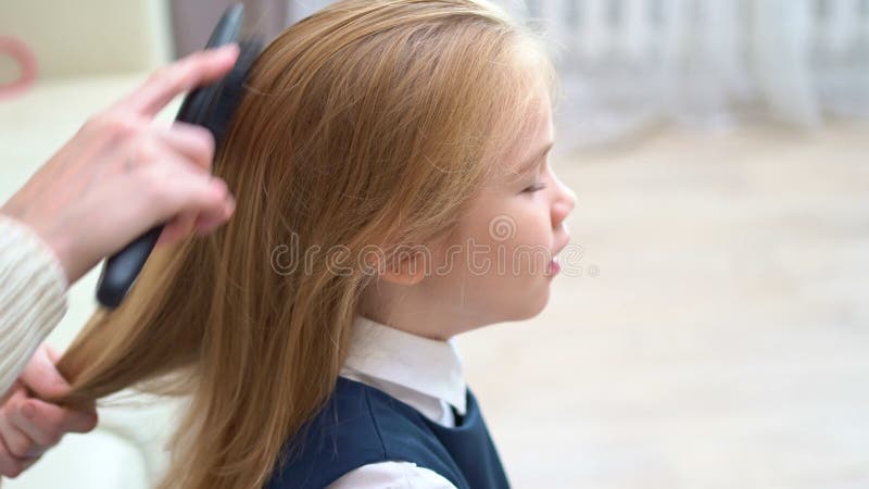 Vista laterale. sbadiglia di una studentessa mentre la madre pettina i capelli. primi aumenti a scuola. video d archivio