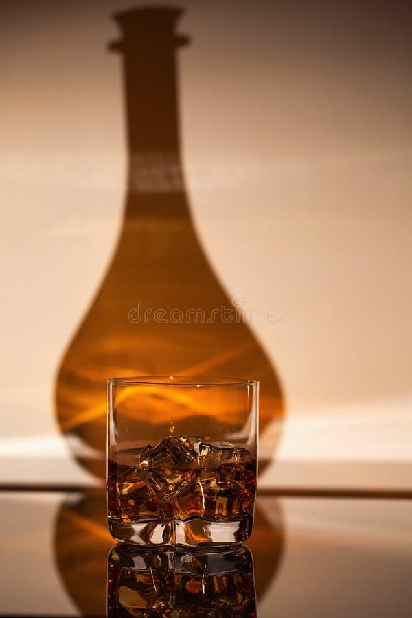 Vista magnífica del vidrio de la bebida del alcohol con hielo en la sombra del fondo de la botella foto de archivo Vista magnífica del vidrio de la bebida del alcohol con hielo en la sombra del fondo de la botella foto de archivo