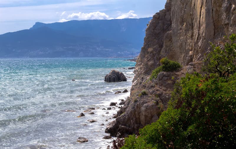 Waves on sea near Yalta with rocks on sea shore and yellow flowers in Crimea. Waves on sea near Yalta with rocks on sea shore and yellow flowers in Crimea