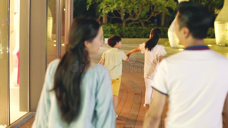 Vista posterior de la familia asiática de 4 que camina en un área de compras en la noche metrajes