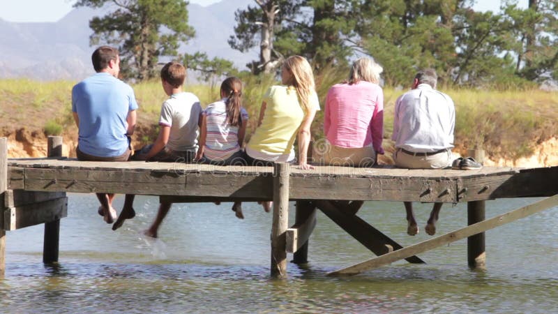 Vista posterior de la familia multigeneración que se sienta en el embarcadero metrajes