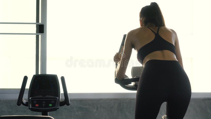 Vista posterior de la mujer deportiva que monta la bici inmóvil en el gimnasio almacen de metraje de vídeo