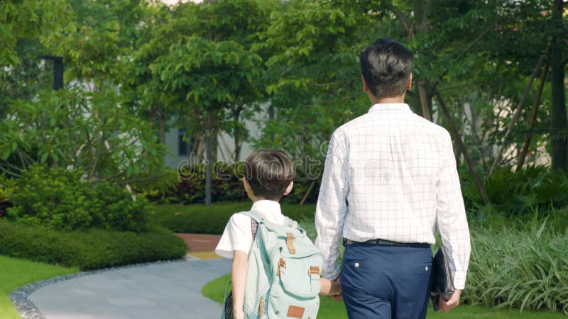 Vista posterior del padre y del hijo asiáticos que van a la cámara lenta de la escuela de lado a lado metrajes