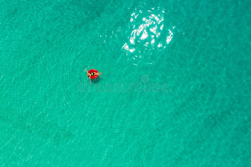 Aerial view of slim woman swimming on the swim ring  donut in the transparent turquoise sea in Seychelles. Summer seascape with girl, beautiful waves, colorful water. Top view from drone. Aerial view of slim woman swimming on the swim ring  donut in the transparent turquoise sea in Seychelles. Summer seascape with girl, beautiful waves, colorful water. Top view from drone