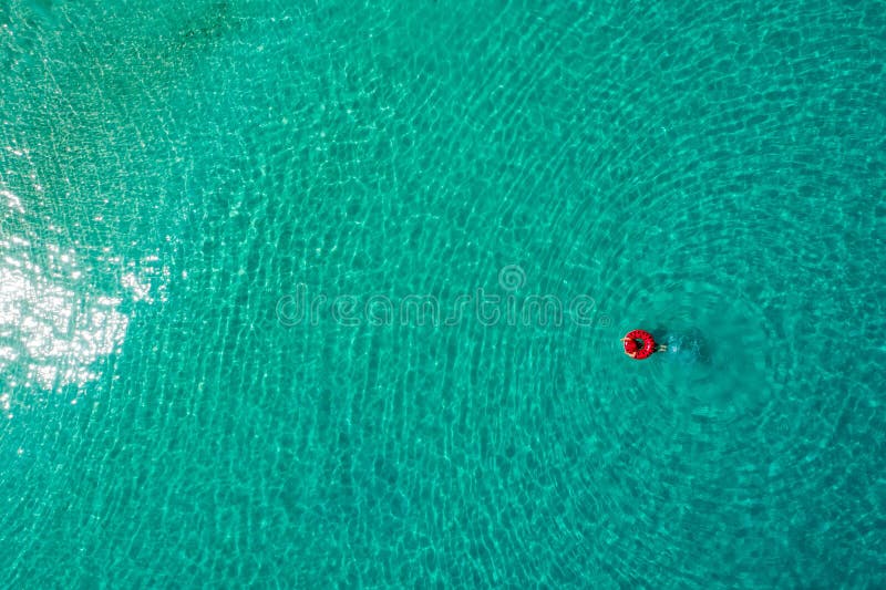 Aerial view of slim woman swimming on the swim ring  donut in the transparent turquoise sea in Seychelles. Summer seascape with girl, beautiful waves, colorful water. Top view from drone. Aerial view of slim woman swimming on the swim ring  donut in the transparent turquoise sea in Seychelles. Summer seascape with girl, beautiful waves, colorful water. Top view from drone