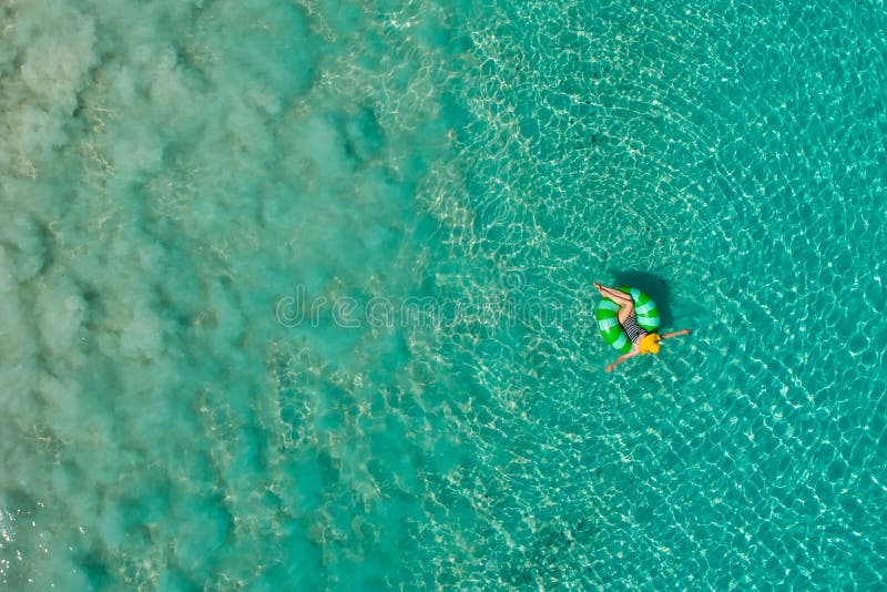 Aerial view of slim woman swimming on the swim ring  donut in the transparent turquoise sea in Seychelles. Summer seascape with girl, beautiful waves, colorful water. Top view from drone. Aerial view of slim woman swimming on the swim ring  donut in the transparent turquoise sea in Seychelles. Summer seascape with girl, beautiful waves, colorful water. Top view from drone